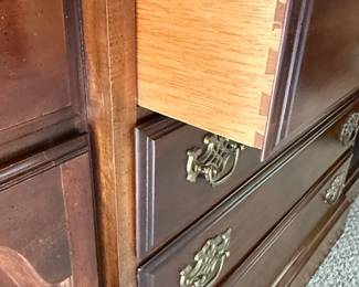 This is a large, traditional china cabinet manufactured by Schwanek Furniture, a company known for its "Fine Interiors" line. The cabinet is constructed from dark-stained wood, likely mahogany or cherry, with a rich, warm finish. It features a multi-paneled glass upper section with decorative mullions forming an intricate diamond pattern, designed to display china and decorative items. The lower section comprises several drawers and cabinets, offering ample storage. The hardware appears to be ornate brass, consistent with traditional furniture styles. The overall aesthetic suggests a piece from the mid to late 20th century, designed to be a focal point in a dining room or living area.