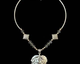 This exquisite necklace features a prominent pendant crafted from iridescent mother of pearl, carved in the shape of a delicate leaf. Adorning the leaf is an intricate silver filigree overlay depicting a stylized flower with swirling tendrils, evoking a sense of organic beauty and artisanal craftsmanship. The pendant hangs from a choker-style necklace composed of a smooth, silver-toned metal wire, interspersed with faceted clear crystal beads and small, round silver beads. The necklace is secured with a toggle clasp. The combination of the natural luminescence of the mother of pearl and the detailed silverwork creates a piece that is both elegant and distinctive, suitable for various occasions.