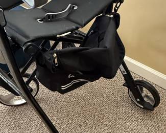 This is a Drive Nitro "Sprint" rollator walker, designed for mobility assistance. It features a lightweight aluminum frame in a black finish, with a padded seat and backrest for comfort. The rollator has large 6-inch front and rear casters for smooth maneuverability over various surfaces. It includes adjustable ergonomic handles, a removable storage pouch, and a cup holder. The "Sprint" model is known for its compact and lightweight design, making it easy to fold for transport and storage.