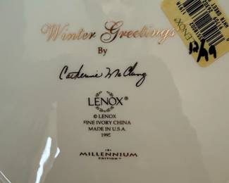This Lenox plate, part of the Millennium Edition, features the 'Winter Greetings' design by artist Catherine McClung. The plate is crafted from fine ivory china and made in the U.S.A. The front of the plate depicts a festive winter scene with a wreath of pine, holly, and mistletoe, adorned with a red ribbon and featuring a cardinal and a chickadee. The rim is accented with a delicate gold band. The back of the plate displays the artist's signature, the Lenox logo, and details about the edition and year of production, 1995. This is specifically a dinner plate, as indicated by the size and the label on the back.