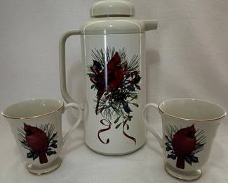This Lenox Winter Greetings set features a white Fine Ivory China teapot and two cups, each adorned with a cardinal perched amidst holly and berries. The teapot has a distinctive quilted pattern on its body and a decorative finial. The cups share the same festive motif and are accented with a gold rim. The set is made of fine ivory china, known for its durability and translucent quality. The design evokes a classic holiday or winter theme. The maker's mark on the cups indicates 'Lenox Fine Ivory China, Made in U.S.A., 1995'.