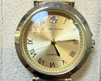 This Adrienne Vittadini women's watch features a gold-tone stainless steel case and bracelet, offering a classic and elegant aesthetic. The champagne dial is adorned with Roman numerals for the hours, and a single diamond accent at the 12 o'clock position signifies luxury. The watch is powered by a quartz movement and is water-resistant, indicated by markings on the case back. The overall design is a blend of traditional watchmaking with modern styling, suitable for both casual and formal wear.