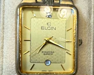 This Elgin Diamond Quartz watch features a rectangular gold-tone case and a champagne-colored dial with a textured guilloché pattern. The dial has applied gold-tone hour markers, a date window at the 6 o'clock position displaying '18', and a single diamond accent at the 12 o'clock position. The watch is powered by a Japan Movt quartz movement and is housed in a base metal bezel with a stainless steel back. The accompanying bracelet is also gold-tone metal, with a link design consistent with watches from the late 20th century. The overall aesthetic suggests a dress watch from the 1980s or 1990s.