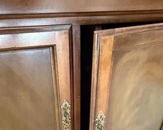 This American Drew sideboard, part of the "American Independence Collection," is crafted from rich, dark wood, likely mahogany or a high-quality veneer, showcasing a traditional style. It features a central drawer with ornate brass hardware, flanked by two cabinet doors with inset panels that exhibit subtle wood grain patterns. The base has a decorative, stepped plinth, and the overall construction suggests a durable and elegant piece of furniture. The "American Independence Collection" line is inspired by the original furnishings of Independence Hall, aiming to capture a sense of historical significance and classic American design. The brass hardware, with its intricate scrollwork, complements the dark wood finish, creating a piece that is both functional and decorative.