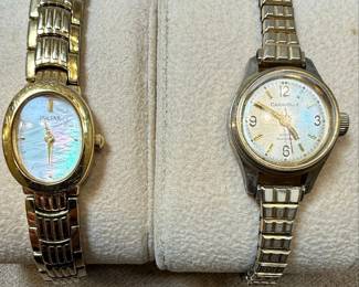This lot features two women's wristwatches: a gold-tone Pulsar with a mother-of-pearl dial and a silver-tone Caravelle with a white dial. The Pulsar watch has an oval case and a multi-link bracelet, with 'PULSAR', 'WATER RESISTANT', 'ST. STEEL', '1N00-X139 R2', 'MOVEMENT JAPAN', and '500106' visible on the case back. The Caravelle watch has a round case, Roman numerals, and a metal expansion band, with 'CARAVELLE', 'WATER RESISTANT', and 'T SWISS T' visible on the dial. Both appear to be quartz-powered and show signs of wear consistent with age and use.