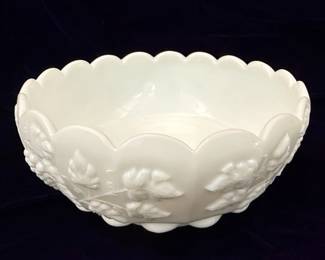 A white milk glass bowl featuring a raised relief pattern of grape clusters and leaves encircling the exterior. The bowl has a scalloped rim and is supported by three integrated feet. The pattern is identified as 'Paneled Grape' and the maker's mark visible in the images is that of Westmoreland Glass.