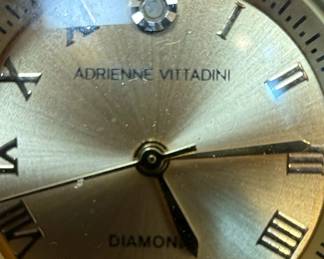 This Adrienne Vittadini women's watch features a gold-tone stainless steel case and bracelet, offering a classic and elegant aesthetic. The champagne dial is adorned with Roman numerals for the hours, and a single diamond accent at the 12 o'clock position signifies luxury. The watch is powered by a quartz movement and is water-resistant, indicated by markings on the case back. The overall design is a blend of traditional watchmaking with modern styling, suitable for both casual and formal wear.