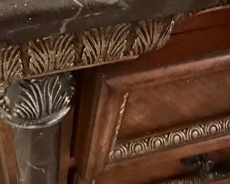 This bedroom set, comprising a tall chest of drawers, a nightstand, and a dresser with a mirror, is crafted from cherry wood with a rich, warm finish. The style is reminiscent of Italian Baroque, characterized by ornate carvings, scrolled hardware, and decorative inlays. Each piece features faux marble columns with detailed capitals and bases, adding a touch of opulence. The dresser top and nightstand top appear to be made of real marble, likely black with white veining, providing a durable and luxurious surface. The intricate detailing on the drawer fronts and the central decorative panel of the dresser suggests a high level of craftsmanship, typical of furniture designed to make a statement.