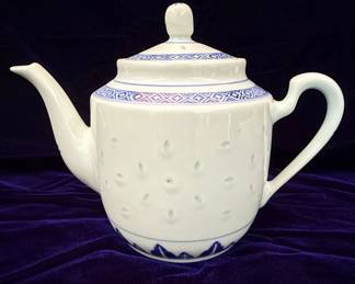 This is a Chinese Export porcelain teapot, likely produced in the mid to late 20th century, as indicated by the 'Made in China' mark. The teapot features a classic silhouette with a gracefully curved spout and handle. Its body is adorned with a pierced lattice pattern, a technique known as 'rice grain' or 'ling lung' porcelain, which allows light to pass through, creating a delicate visual effect. The decoration consists of intricate blue and white patterns, including a geometric band around the shoulder and a floral motif near the base. The glaze appears smooth and glossy, typical of porcelain. No obvious defects are visible in the provided images.