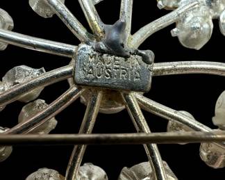 This set features two distinct vintage brooches, both likely dating from the mid-20th century. The larger brooch showcases a bouquet design with three lustrous faux pearls nestled among swirling, pave-set rhinestones that mimic the sparkle of diamonds. Its silver-tone metal setting is intricately detailed, with flowing ribbons and leaf-like elements. The second brooch is a starburst or snowflake design, radiating from a central, larger rhinestone, with smaller stones and clear crystals forming delicate branches. The reverse of the starburst brooch clearly indicates 'MADE IN AUSTRIA', a mark associated with high-quality costume jewelry production from that region. Both pieces are crafted from silver-tone metal, likely a base metal alloy, and are adorned with prong-set rhinestones and faux pearls. The overall aesthetic leans towards Art Deco or Mid-Century Modern styles, popular during their likely period of creation.