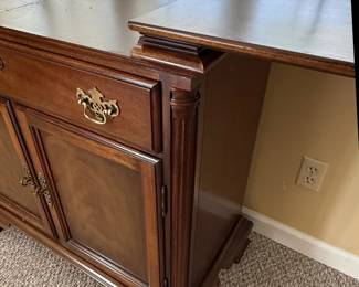 This American Drew sideboard, part of the "American Independence Collection," is crafted from rich, dark wood, likely mahogany or a high-quality veneer, showcasing a traditional style. It features a central drawer with ornate brass hardware, flanked by two cabinet doors with inset panels that exhibit subtle wood grain patterns. The base has a decorative, stepped plinth, and the overall construction suggests a durable and elegant piece of furniture. The "American Independence Collection" line is inspired by the original furnishings of Independence Hall, aiming to capture a sense of historical significance and classic American design. The brass hardware, with its intricate scrollwork, complements the dark wood finish, creating a piece that is both functional and decorative.