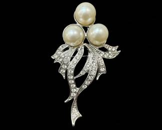 This set features two distinct vintage brooches, both likely dating from the mid-20th century. The larger brooch showcases a bouquet design with three lustrous faux pearls nestled among swirling, pave-set rhinestones that mimic the sparkle of diamonds. Its silver-tone metal setting is intricately detailed, with flowing ribbons and leaf-like elements. The second brooch is a starburst or snowflake design, radiating from a central, larger rhinestone, with smaller stones and clear crystals forming delicate branches. The reverse of the starburst brooch clearly indicates 'MADE IN AUSTRIA', a mark associated with high-quality costume jewelry production from that region. Both pieces are crafted from silver-tone metal, likely a base metal alloy, and are adorned with prong-set rhinestones and faux pearls. The overall aesthetic leans towards Art Deco or Mid-Century Modern styles, popular during their likely period of creation.