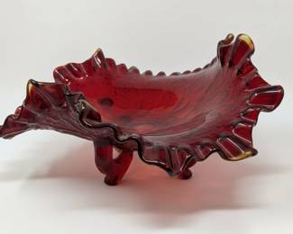 This exquisite vintage bowl is crafted from rich ruby red glass, featuring a striking ruffled rim that adds a touch of elegance and movement. The glass is pressed with a detailed leaf or floral motif, visible within the bowl's interior, suggesting a decorative purpose. It stands on three small, rounded feet, elevating it slightly and contributing to its unique silhouette. The color transitions from a deep, opaque red to a more translucent, amber hue at the very tips of the ruffles, a characteristic often seen in art glass of the mid-20th century. Its overall design evokes a sense of Victorian or Art Nouveau influence, making it a captivating piece for display or use as a decorative accent.