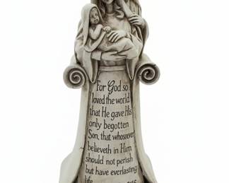 This figurine depicts the Holy Family: Mary holding the infant Jesus, with Joseph standing behind them. The piece is designed to resemble aged stone or plaster and features an inscription of John 3:16 on a scroll that forms the base. The style is devotional and commemorative, common in religious home decor. The material appears to be resin or a similar composite, finished to mimic a weathered, monochromatic look. The inscription is clearly legible, adding a significant biblical element to the piece. The overall dimensions are approximately 8 inches in height and 4 inches in width.