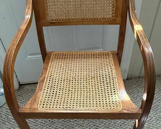 This armchair features a bentwood frame, characteristic of mid-century modern design, with a warm wood finish. The seat and backrest are intricately woven with natural cane, offering a classic and breathable design. The chair's silhouette is characterized by gently curved arms that flow into the front legs, and the back legs are slightly splayed for stability. The overall style evokes a sense of mid-century modern design, suitable for various interior settings. The cane webbing shows a typical hexagonal pattern, indicating a traditional weaving technique.