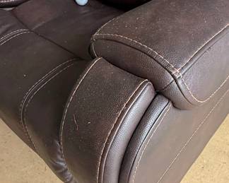 This is a brown, faux leather power lift recliner chair. It features plush, overstuffed cushioning with decorative stitching in a contrasting cream color. The chair is operated by a wired remote control that allows for adjustment of the headrest and back, as well as a lift function, indicated by directional arrows on the remote. The remote also has buttons for headrest and back adjustments, suggesting multiple reclining positions and lumbar support options. The material appears to be a durable, easy-to-clean faux leather, suitable for everyday use. The overall design is contemporary and emphasizes comfort and ease of use, particularly for individuals who may require assistance with standing or sitting.