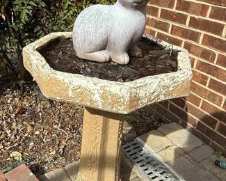 This vintage garden piece features a decorative bird bath with an attached seated rabbit figurine. The bird bath itself has an octagonal basin with a distressed, aged finish, appearing to be painted a light cream color over a darker base, showing signs of wear and chipping. The basin is adorned with relief carvings of floral swags. The pedestal base is also octagonal and features vertical fluting with decorative relief elements, including floral motifs and draped fabric designs. The entire piece is crafted from concrete or a similar cast stone material, giving it a weathered, aged appearance suitable for outdoor garden decor. The rabbit figurine, seated within the basin, is also made of concrete and has a textured, stone-like finish, with simple, stylized features. The overall aesthetic suggests a classical or traditional garden style, likely dating from the mid to late 20th century. The rabbit is depicted in a seated position, adding to its charm.