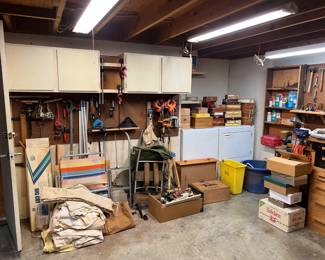 On top of the washer and dryer are a collection of cigar boxes.  There is a vintage external frame backpack.  There are clamps on the wall near the cabinets.
