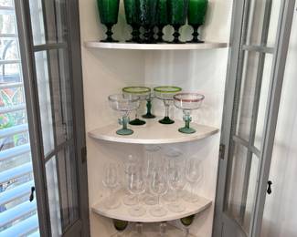 Ballard design glass door corner cabinet in a gray finish, which is Pinewood a bow front with curved glass cabinet door. Measure measures 74 inches tall by 30 inches wide by 15 1/2 inches deep.