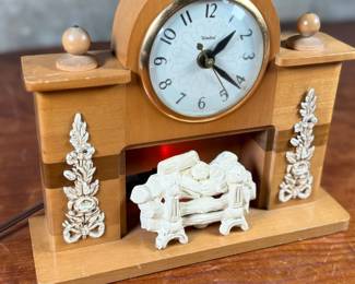 This lot features a vintage United Clock Corp. electric fireplace mantle clock, likely from the 1940s or 1950s in good working condition. This clock has a wooden case with white floral decorative accents on the uprights and a simulated log fireplace scene. 