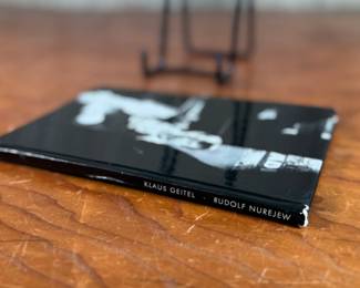 This lot features a rare, pocket-sized collectible book titled “RUDOLF NUREJEW” by German ballet critic Klaus Geitel. The book focuses on the famous ballet dancer Rudolf Nureyev at the height of his career and is signed on the front by Nureyev himself. The book is published by Rembrandt Verlag and comes in good overall condition.