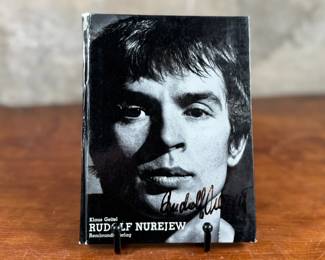 This lot features a rare, pocket-sized collectible book titled “RUDOLF NUREJEW” by German ballet critic Klaus Geitel. The book focuses on the famous ballet dancer Rudolf Nureyev at the height of his career and is signed on the front by Nureyev himself. The book is published by Rembrandt Verlag and comes in good overall condition.