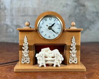 This lot features a vintage United Clock Corp. electric fireplace mantle clock, likely from the 1940s or 1950s in good working condition. This clock has a wooden case with white floral decorative accents on the uprights and a simulated log fireplace scene. 