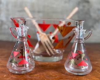 This lot features a rare mid-century Gay Fad "Moon" pattern set circa 1950s featuring atomic-style red and gold triangles and dots. The set includes a clear glass serving bowl, matching wooden serving utensils, and two glass cruets with stoppers. One of the stoppers has damage as shown in photos.