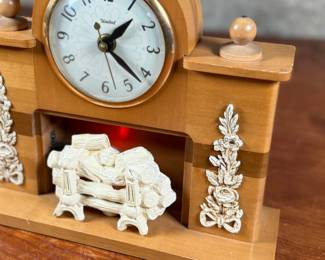 This lot features a vintage United Clock Corp. electric fireplace mantle clock, likely from the 1940s or 1950s in good working condition. This clock has a wooden case with white floral decorative accents on the uprights and a simulated log fireplace scene. 