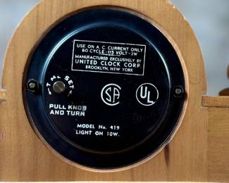 This lot features a vintage United Clock Corp. electric fireplace mantle clock, likely from the 1940s or 1950s in good working condition. This clock has a wooden case with white floral decorative accents on the uprights and a simulated log fireplace scene. 