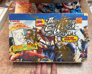 This image shows a Marvel Comics The Silver Age hobby box of trading cards, which is a collectible item. 
This box contains 36 packs. 
Marvel trading cards, iconic characters from the "Silver Age" era of comics. 
These boxes are known to guarantee one hand-drawn sketch autograph card in every box.
ON EBAY FOR $1,400 EACH MINIMUM *WOW*