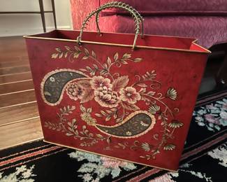 decorative red metal magazine holder with hand-painted floral and paisley details and twisted wire handles. 

