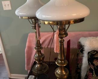 pair of vintage Stiffel brass hurricane lamps with milk glass shades, featuring a classic mid-century design. 
Manufacturer: Stiffel Company.
Style: Mid-Century Modern.
Materials: Solid brass base and milk glass shade.
Features: Includes tassels and a traditional hurricane-style glass chimney.
