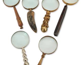 2105 A group of six magnifying glasses Late 19th/20th century One with partial mark impressed to rim: SWIFT & ANDERSON INC / BOSTON Comprising one Swift & Anderson with leather-clad handle and gilt-tooled cover, one with brass-inset wood handle, one with brass figural handle, one turned brass, one carved horn, and one nickel-plated metal 6 pieces Largest: 12.75" L x 4.5" Dia.; Each glass: 4" Dia. Estimate: $400 - $600