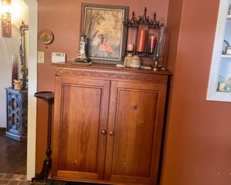 Vintage wood armoire with intricate carving detail, sitting on scrolled wrought iron stand with integrated storage rack