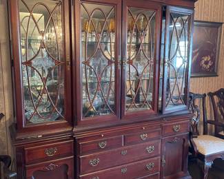 Stonleigh breakfront display china cabinet in traditional Georgian Chippendale style high quality mahogany wood. Hutch features 4 glazed glass doors with elegant curved fretwork, adjustable shelves and interior lighting, carved scrollwork pediment on top. Lower buffet includes 6 dovetailed drawers and 2 side cupboards and antique style brass