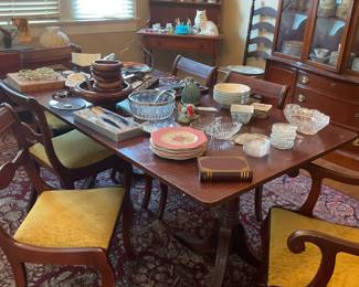 Large wooden dining table with six chairs, one being a captain chair. Misc kitchen items, teak salad bowl set, beautiful rug, crystal, napkin rings, place setting name plates, serving sets, and gorgeous trivet. 