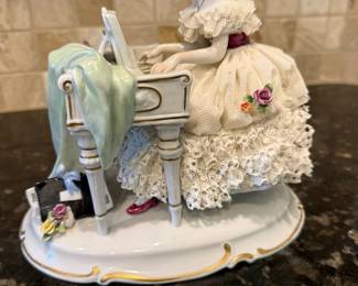 This vintage collectible figurine is a German porcelain "Dresden Lace" scene depicting a woman playing a piano