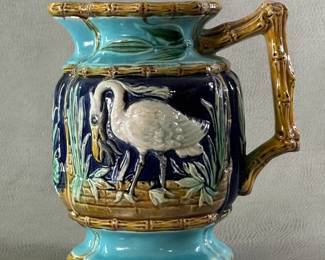 Another view of the American majolica pitcher circa 1880-90; heavy cast, molded pitcher with raised cranes painted white against a cobalt blue background against a low brick wall; four borders of tan bamboo, top/bottom rim and end handle also of bamboo design.