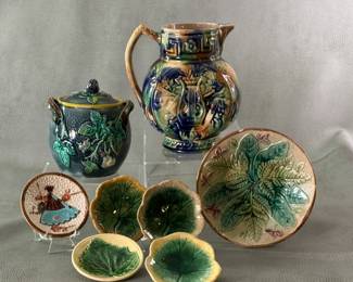 Antique and vintage majolica including Griffin, Smith & Hill butter pats, a lidded jam jar with blackberry pattern and finial, and a circa 1885-90 American majolica ware cream pitcher, 6" high, unusual jug with Greek key fret decoration around the neck, high relief lyre/musical instruments on the body; hand-painted in blue, brown, green and mauve applied in dabbing streaking manner, pale lavender liner.