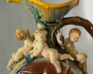 Closeup of the stunning rare 1861 large hand-painted majolica ewer, 14-1/2" tall, marked Minton, known as the Palissy jug, modeled by French sculptor Hughes Protat with impressed modeler’s initials HP under handle; formed as barrel, the neck adorned with 4 festive cherubs, circular body decorated w/raised green brown vine tendrils, deep turquoise liner, prof. repair to handle.
