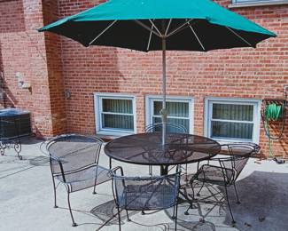 An outdoor patio furniture set comprised of a dark green market umbrella, and 4 black mesh metal dining chairs and table