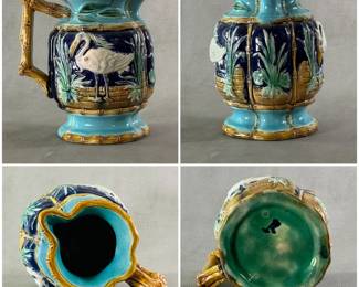 An American majolica pitcher circa 1880-90; heavy cast, molded pitcher with raised cranes painted white against a cobalt blue background against a low brick wall; four borders of tan bamboo, top/bottom rim and end handle also of bamboo design.