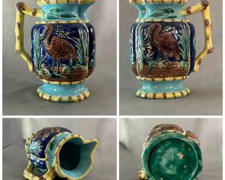 An American majolica pitcher circa 1880-90; heavy cast, molded pitcher with raised cranes painted brown against a cobalt blue background against a low brick wall; four borders of yellow bamboo, top/bottom rim and end handle also of bamboo design.