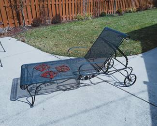 A mid-century modern Woodward style black wrought iron chaise lounge chair with mesh design, adjustable reclining back, and wheels for mobility