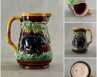 A small majolica pitcher, 6-3/4" high, circa 1880, with highly glazed hand painted grey elephants and green palm like trees in relief on dark brown ground. Golden bamboo design handles, lavender liner. Base with four underglaze brown dots.