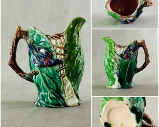A majolica pitcher circa 1880-90, pitcher of high glazed green ground in shape of cauliflower leaves being laced together by high relief bird; birds are hand colored in cobalt blue, deep pink, green, yellow. Brown bark handle and lavender liner. 7-1/2 inch tall.