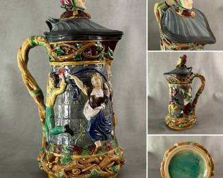 A rare Minton Majolica "Tower" jug or tankard, 13” H, featuring medieval dancing scene and a jester finial on the pewter mounted lid. Designed by Hugues Protat, one of the most highly regarded majolica artists at Minton. Moulded cylindrical body representing facade of a castle w/dancing medieval men and women in relief between two bands of twining ivy stems which extend to form the handle. The base w/impressed “MINTON”, factory mark, date mark for 1869, and numerals '1231'.