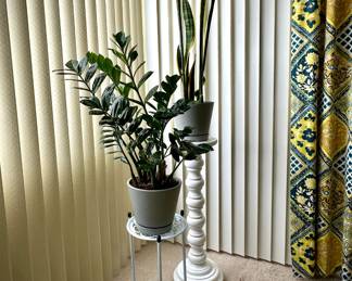 A 2-tier white metal plant stand featuring a decorative circular lattice design on its shelves, and a large white candlestick style plant stand