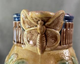 Closeup of the butterfly spout on the antique Griffin, Hill & Smith majolica pitcher circa 1880-1890, with butterfly spout, basketweave base and wild rose pattern on body, hand-colored in pale yellow ground with pink flowers and green leaves; brown basketweave trim and butterfly, cobalt blue top rim, lavender/pink liner. Marked with double circle trademark of GHS Etruscan Majolica